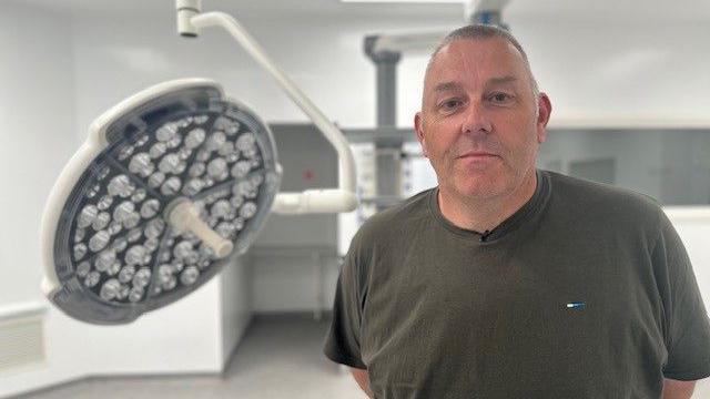 Patient Jason Sykes, wearing a khaki t-shirt, stands in the new operating theatre.