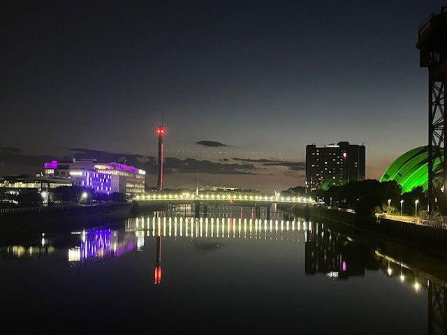 Buildings are lit green and purple in the distance, with the River Clyde stretching between them and going into the distance