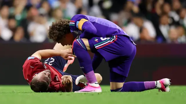 Guillermo Ochoa, wearing Mexico's purple goalkeeping kit, attends to Tomas Soucek, wearing the Czech Republic's red kit, who lies on the pitch in pain after suffering an injury