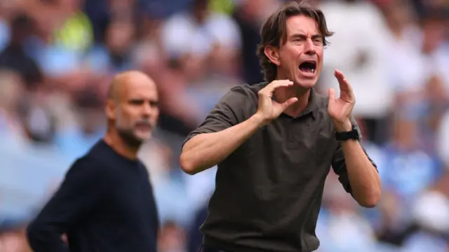 Thomas Frank shouts instructions to his players from the sidelines as Manchester City manager Pep Guardiola watches behind him