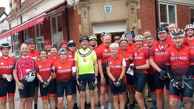 A group of about 25 people in red cycling jerseys, dark shorts and cycling helmets. In the centre is mayor Andy Gilbert who is wearing a yellow jersey and the mayoral civic chains of office around his neck