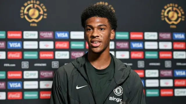 Josh Acheampong wearing a Chelsea training top in front of a background of various sponsors’ logos