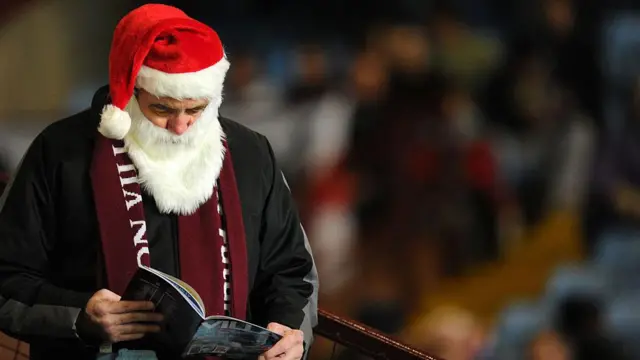 Someone dressed as Santa reading an Aston Villa programme