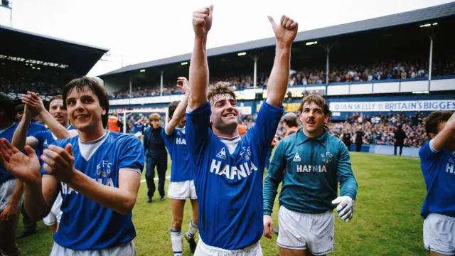 Kevin Ratcliffe holds his arms aloft in front of the crowd at Goodison Park, with Everton team-mates Neville Southall and Graeme Sharp either side of him