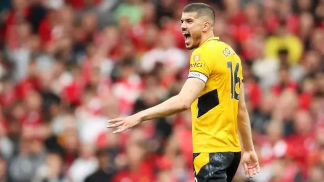 Conor Coady, wearing Wolves' gold home shirt and shouting instructions to team-mates during a match when he was captain