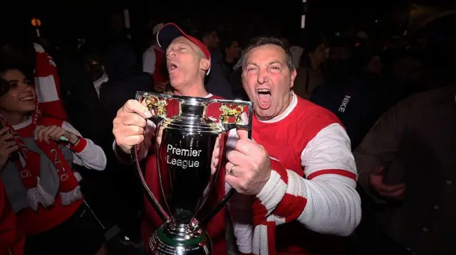 Arsenal fans clutch a Premier League trophy in celebration