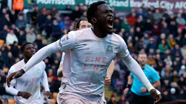 Brendan Wiredu run with his arms out wide and his eyes closed and mouth open in celebration after scoring a goal for Plymouth Argyle
