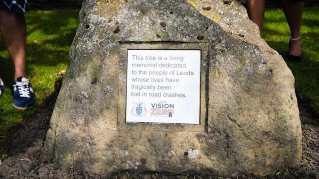 A white plaque on a rock, with the message: "This tree is a living memorial to the people of Leeds whose lives have tragically been lost in road crashes."