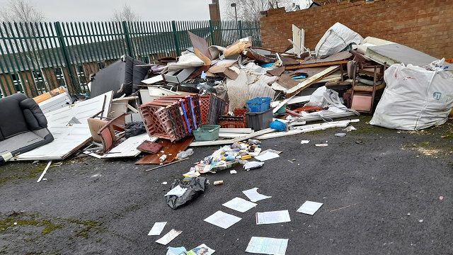 Fly-tipping in a yard including plastic crates and furniture