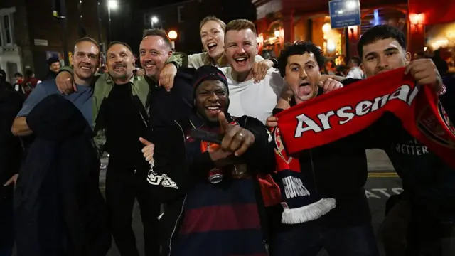 Arsenal fans celebrate in a huddle by their stadium