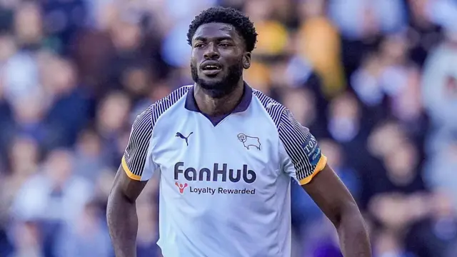 Patrick Agyemang, wearing Derby's white home shirt, stands on the pitch against Stoke City