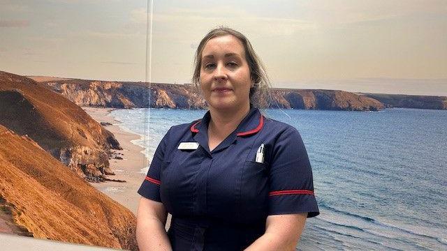 A nurse in a blue nurses uniform standing in front of a picture of a beach scene