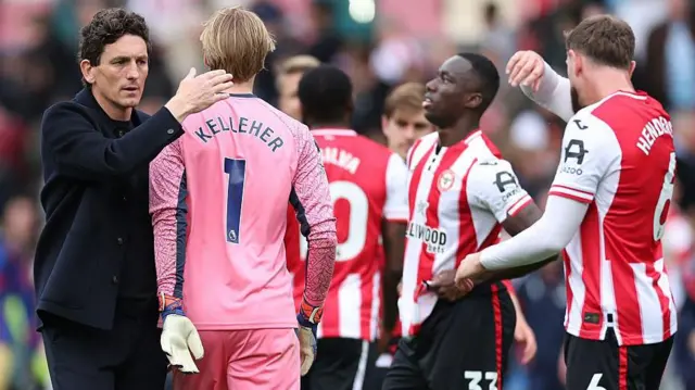 Keith Andrews pats Caoimhin Kelleher on the back of his head as other Brentford players look disappointed in the background