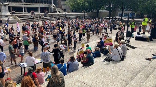 Campaigners in Portsmouth city centre  sitting, standing, listening and holding placards