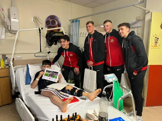 Players from Sunderland's men team with a young boy in his hospital bed holding up a signed photo