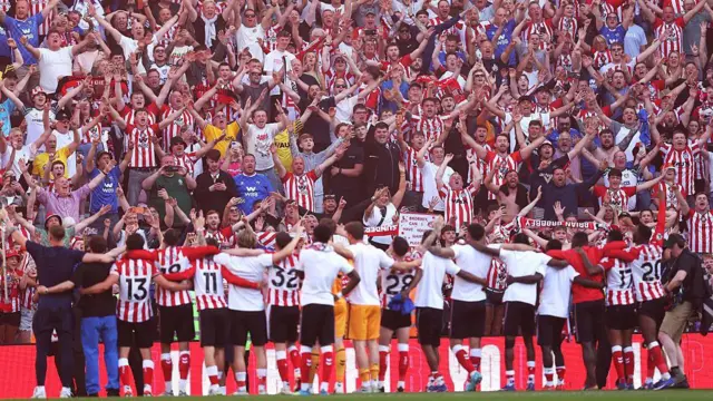 Sunderland players with their arms round each other in front of a stand full of celebrating supporters