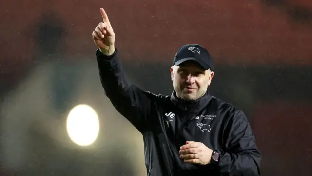 John Eustace holds one arm in the air with his index finger pointed as he stands facing the Derby County fans in the away end while walking on the pitch at Ashton Gate at full-time