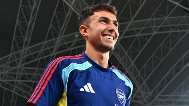 A smiling Martin Zubimendi looks into the distance pre-season game, wearing an Arsenal training top