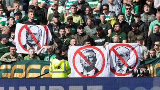 Celtic fans hold up flags against Michael Nicholson, Dermot Desmond and Peter Lawwell