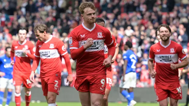 Tommy Conway, wearing Middlesbrough's red home shirt, pumps his fist out in front of him to celebrate scoring against Watford. His team-mates can be seen behind running after him to celebrate.