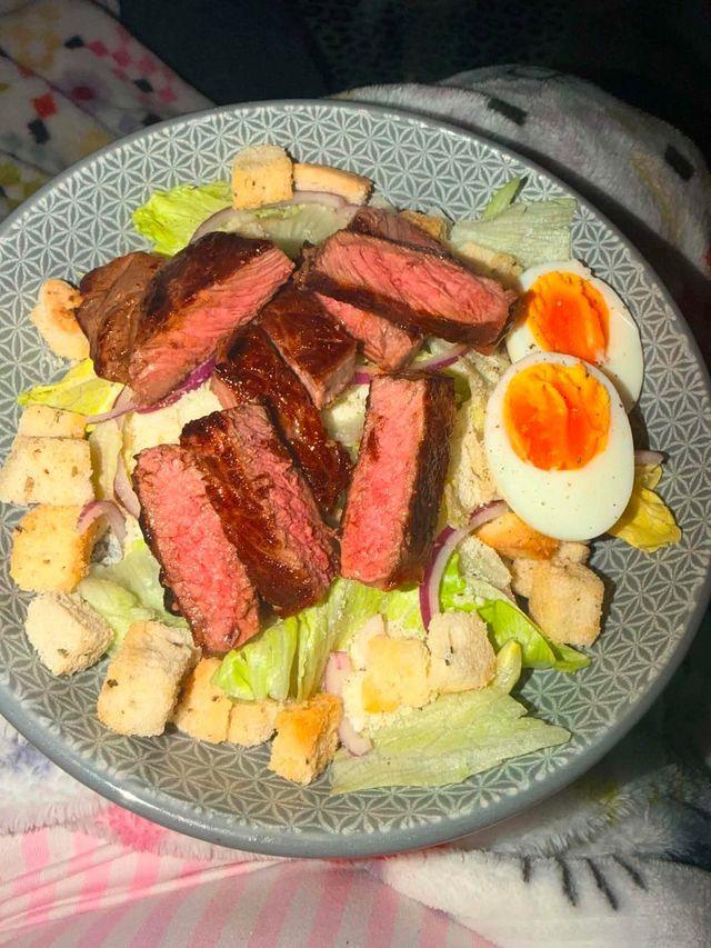 A plate with sliced cook steak, boiled eggs, crutons and lettuce