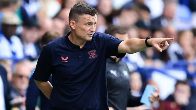 Preston boss Paul Heckingbottom in a dark blue polo top pointing to his players on the touchline