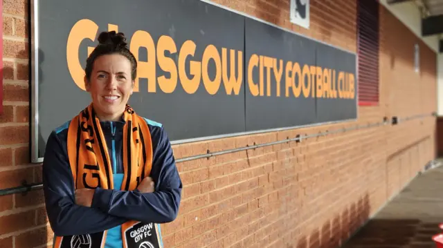 Leanne Crichton standing at a Glasgow City FC sign