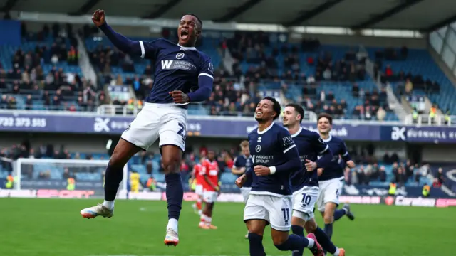 Aidomo Emakhu jumping in the air while celebrating his goal for Millwall with his team-mates running up to congratulate him