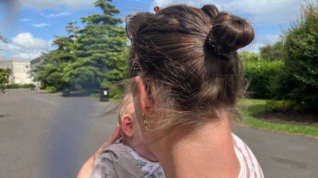 Louise, a'i chefn tua'r camera, yn cydio yn ei babi - mae hi'n dymuno aros yn anhysbys ac ddim am i'w hwynebau gael eu dangos