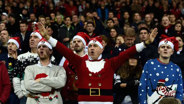 Bournemouth fans in Christmas Jumpers and Bournemouth Santa hats singing at a match