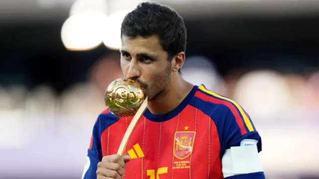 Rodri in a Spannish jersey kissing the Golden Ball trophy.
