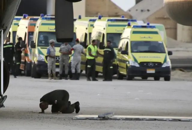 An Egyptian soldier prays as emergency workers prepare to unload bodies of victims from the crash of a Russian aircraft over the Sinai peninsula from a police helicopter to ambulances at Kabrit military airport, some 20 miles north of Suez, Egypt, on 31 October 2015.