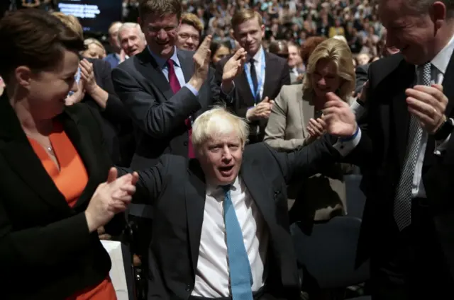 Boris Johnson sits as those around him applaud on their feet