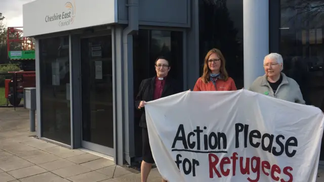 Three people holding banner for 'action please for refugees'