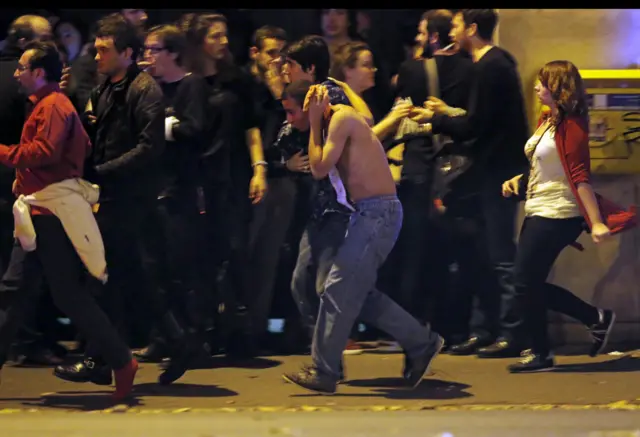 An injured man holds his head as people gather near the Bataclan concert hall following fatal shootings in Paris