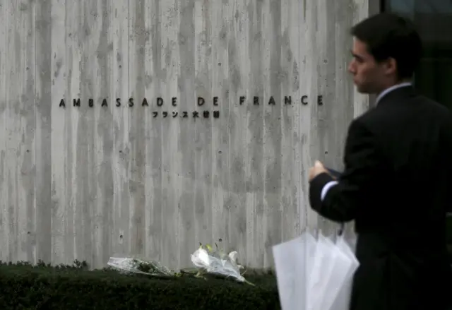 A man walks past bunches of flowers at the French embassy in Tokyo