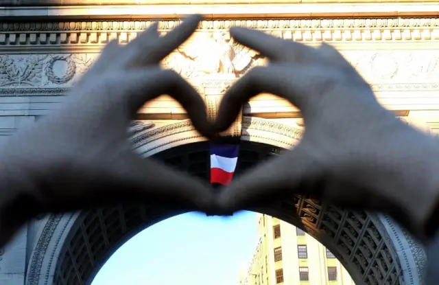 A woman makes a heart shape, enclosing the French flag