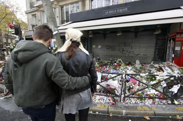 A couple share a quiet moment in front of flowers, candles and messages in tribute to victims in front of the La Belle Equipe cafe, one of the sites of the deadly attacks in Paris