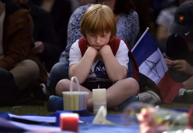 A young French supporter sits quietly next to a French flag during a remembrance service in Civic Square for the victims of the Paris terror attacks