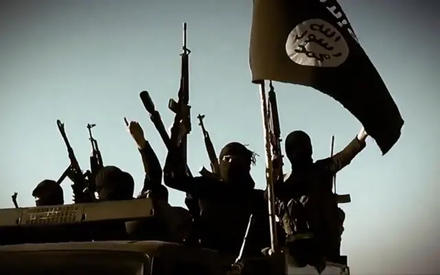 militants raising their weapons as they stand on a vehicle mounted with the trademark Jihadists flag