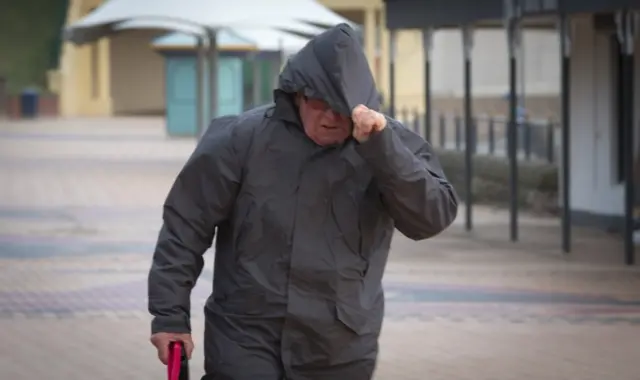 A man pulls his hood down in the wind