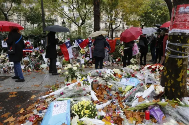 People look at flowers, candles and messages in tribute to victims near the Bataclan concert hall, a week on from the attacks