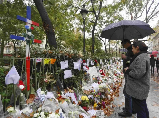 People look at flowers, candles and messages in tribute to victims near the Bataclan concert hall, a week on from the attacks