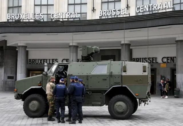 A Belgian soldier and police officers stand next to a military armoured vehicle parked at the entrance of Brussels central train station