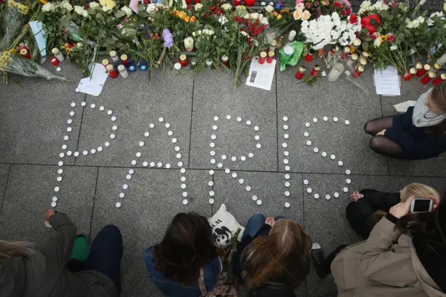 People finish arranging candles into the word 'Paris' next to flowers and messages left at the gate of the French Embassy following the recent terror attacks in Paris on 14 November 2015 in Berlin, Germany