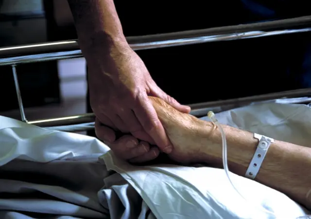 Nurse holds elderly patient's hand