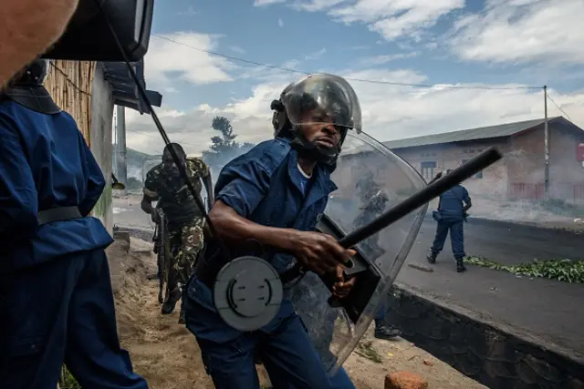 A Burundian police officer holding a baton and army forces run after protestors throwing stones during a demonstration against incumbent president Pierre Nkurunziza's bid for a third term on May 13, 2015 in Bujumbura