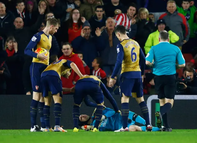 Arsenal players stand over an injured Petr Cech