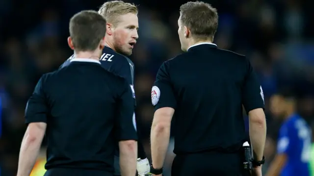 Kasper Schmeichel speaks with referee Craig Pawson as they leave the field at half-time