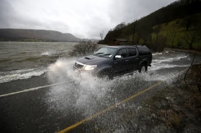 A car pushes on through water across the A592 near Ullswater, Cumbria